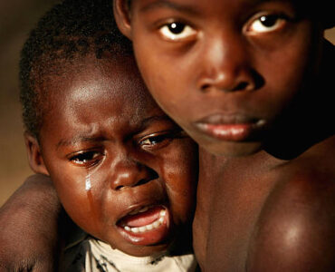 MOZAMBIQUE- JULY 2 :  A one year old orphan sits on his brother's knee crying in a small village outside Quelimane, on July 2, 2005 in, Mozambique. Since Mozambique's 15-year civil war ended in 1992, the country has made a strong recovery. However, it suffered setbacks with severe floods in 2000 and 2001, followed by two years of drought in 2002 and 2003. These emergencies had a huge impact and led to widespread food shortages, an increase in outbreaks of infectious diseases, including cholera, measles and meningitis.  Families in rural areas in particular suffer from poverty and a lack of basic services. About 13 per cent of babies die before their first birthday, 20 per cent of children die before the age of five, and 48 per cent of the country's children are chronically malnourished. The HIV/AIDS pandemic is having a devastating effect on families, with tens of thousands of children orphaned, many of them also HIV-positive or already ill with AIDS.  (Photo by Graeme Robertson/Getty Images)